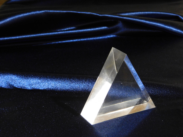 a clear glass triangle-shaped prism sits on a background of dark blue satin.