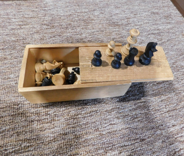 Photo of a small wooden box containing wooden chess pieces.